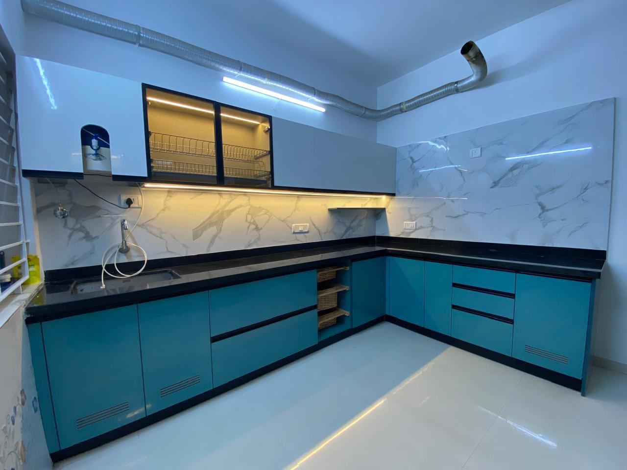 L-shaped modular kitchen with teal cabinets, white marble backsplash and black countertop